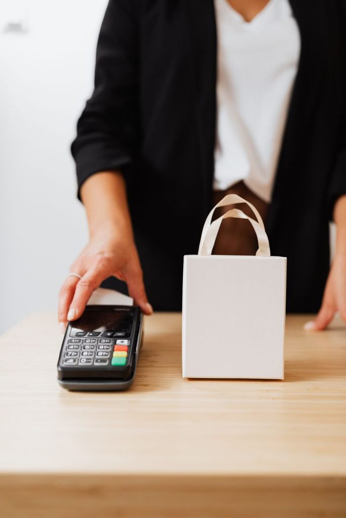 A person making a cashless payment using a terminal and gift bag on the counter.